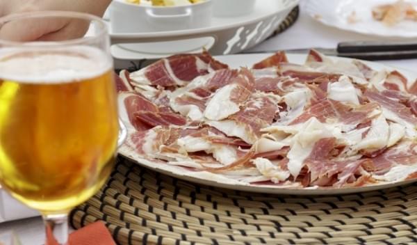 Dish of iberian ham slices beside beer glass and other foods